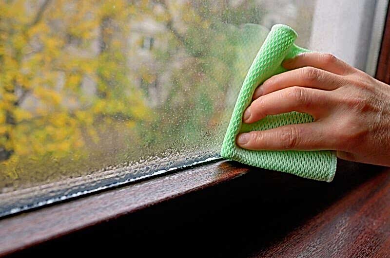 woman wiping condensation from humidity on her window