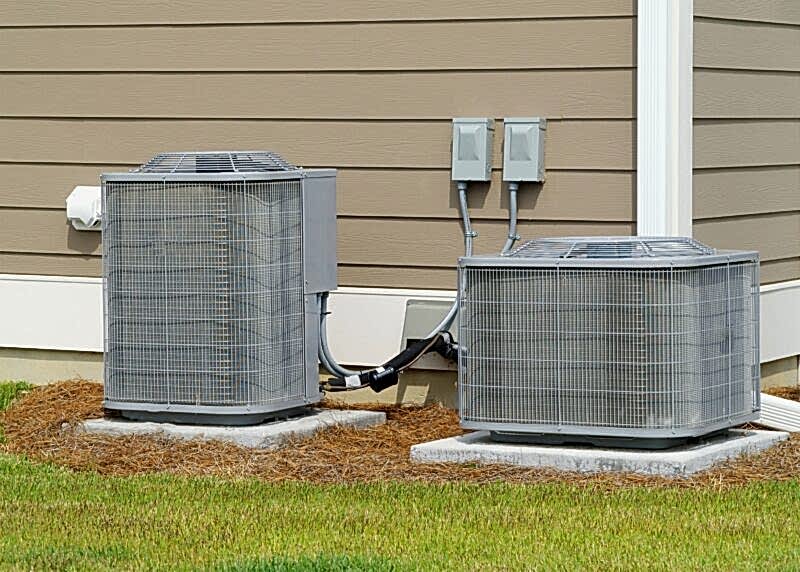 one tall and one short, light gray hvac units installed outside a tan colored home in houston